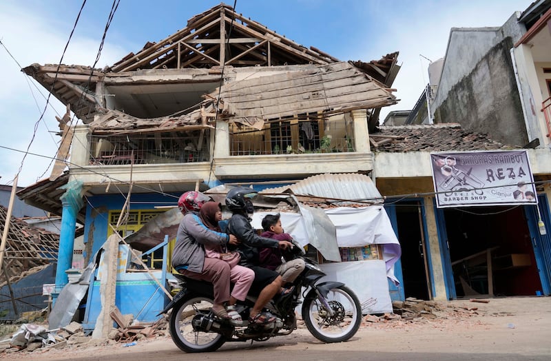 People ride a motorbike past a damaged building in Cianjur. AP