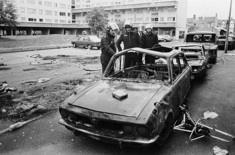 LONDON - OCTOBER 1985: (FILE PHOTO) Police officers in riot gear inspect a burned-out car on the Broadwater Farm housing estate, Tottenham, London, the day after the riot of 6th October 1985. Twenty-Six years later, riots have again broken out in Tottenham on August 6, 2011 following a demonstration protesting the police shooting of twenty-nine-year-old father-of-four Mark Duggan on August 4, 2011 who died in an exchange of gunfire while police were attempting to arrest him.  (Photo by Julian Herbert/Getty Images) *** Local Caption ***  120530699.jpg