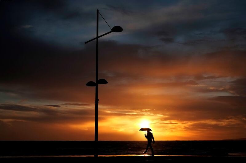 A man walks in the rain as the sun sets in Ayia Napa, Cyprus. Petros Karadjias / AP Photo