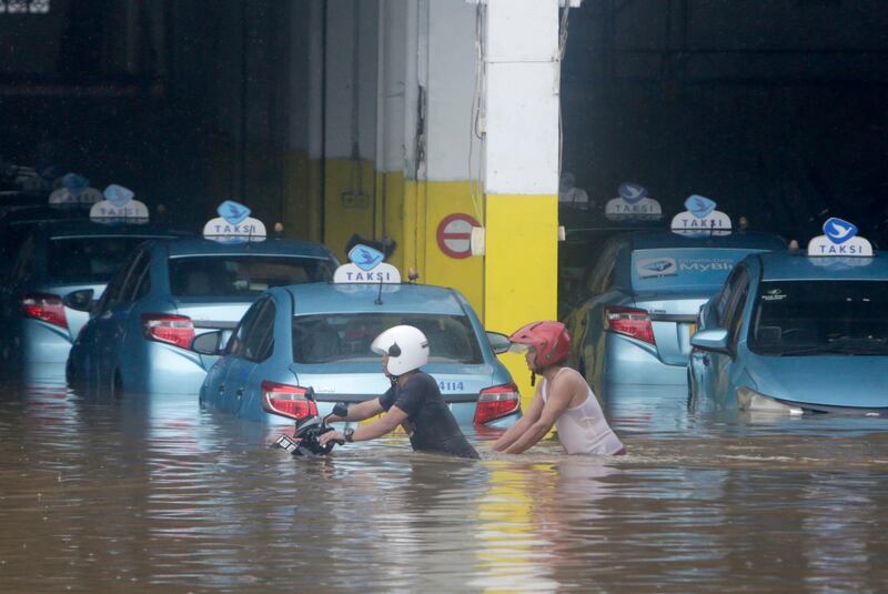 Residents push a motorcycle among submerged taxis on a flooded street in Jakarta, Indonesia. EPA