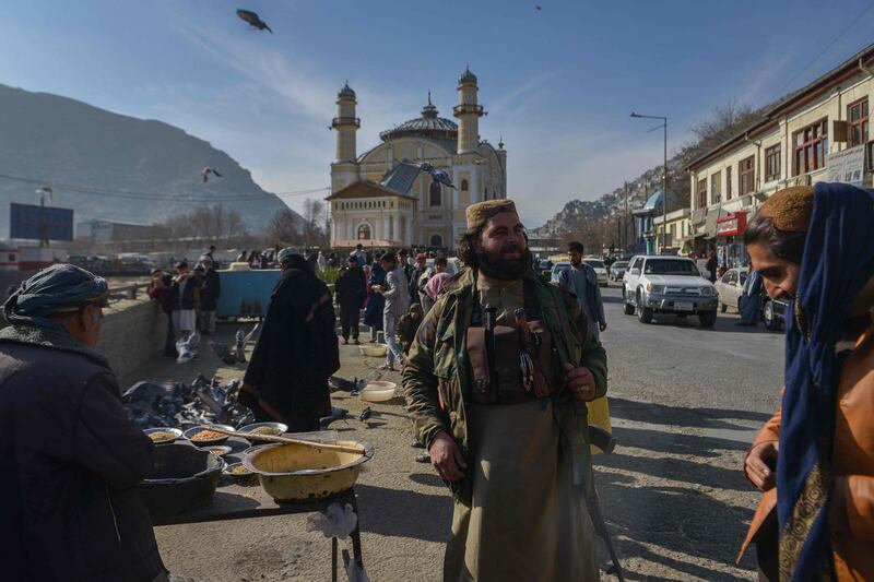 A member of the Taliban stands next to an Afghan hawker selling bird feed at a market area in Kabul. Photo: AFP