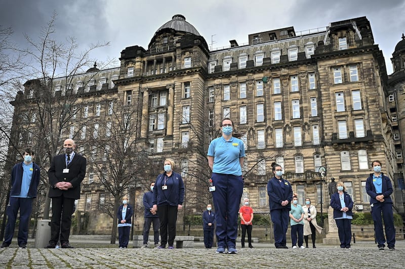 GLASGOW, SCOTLAND - MARCH 23: Staff from the Glasgow Royal Infirmary gather outside the hospital for a minute‚Äôs silence on March 23, 2021 in Glasgow, Scotland. Marie Curie Cancer Charity has organised a National Day of Reflection on the first anniversary of the day Britain entered Coronavirus lockdown, for the UK to come together and remember the 126,000 people who have died from Covid-19. A minutes silence will be held at midday and yellow ribbons tied to trees across the country. (Photo by Jeff J Mitchell/Getty Images)