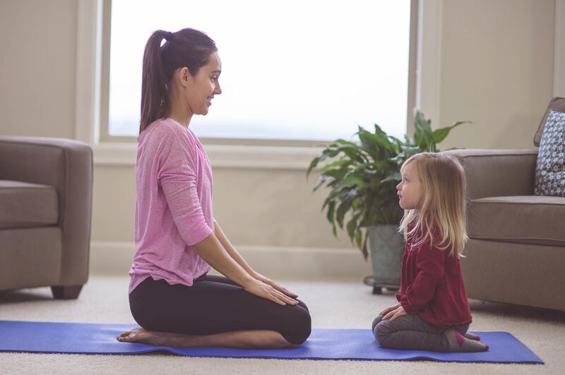 Beautiful young ethnic mom teaches her young daughter yoga. They are kneeling and facing each other. Mom has her hands pressed together and upward. There is a large window in the background in the living room. Getty Images