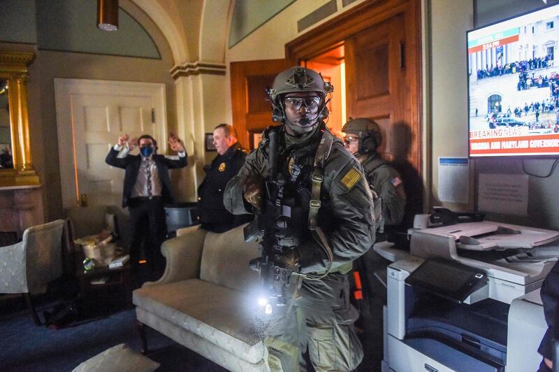 (FILES) In this file photo a Congress staffer holds his hands up while Capitol Police Swat team check everyone in the room as they secure the floor of Trump supporters in Washington, DC on January 6, 2021. A young woman identified as having taken part in the storming of the US Capitol reportedly stole a laptop belonging to top Democrat Nancy Pelosi and hoped to sell it to a Russian spy agency, according to an FBI criminal complaint. The complaint, filed late January 17, 2021 in US District Court in Washington, seeks the arrest of Riley June Williams of Pennsylvania on grounds including "violent entry and disorderly conduct on Capitol grounds." / AFP / Olivier DOULIERY
