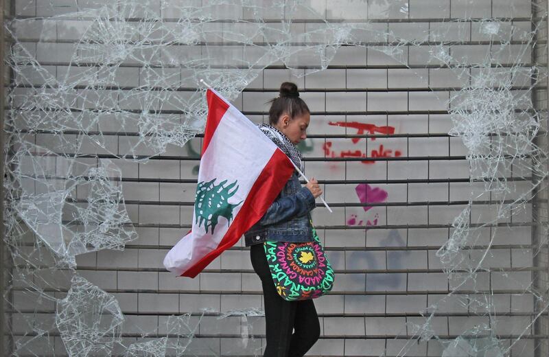 An anti-government protester walks with a Lebanese national flag past a broken window in downtown Beirut. AFP