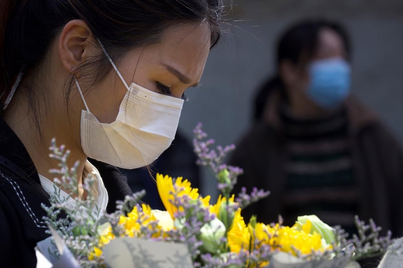 A woman holds a floral bouquet as people gather outside of a park where an official memorial was held for victims of coronavirus in Wuhan in central China's Hubei Province, Saturday, April 4, 2020. With air raid sirens wailing and flags at half-mast, China held a three-minute nationwide moment of reflection to honor those who have died in the coronavirus outbreak. (AP Photo/Ng Han Guan)