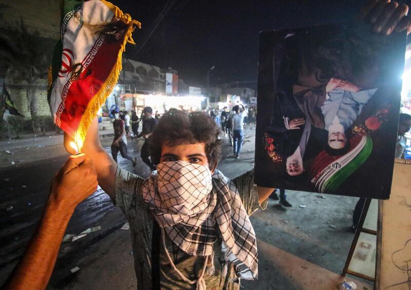 TOPSHOT - An Iraqi protester holds up an Iranian flag as another sets it on fire for him, next to a portrait depicting Iran's former and current Supreme Leaders Ayatollah Khomeini and Khamenei, during demonstrations against the government and the lack of basic services in Basra on September 7, 2018. - Iraqi protesters on Friday torched the Iranian consulate in the southern city of Basra on September 7 in fresh demonstrations over poor public services after parliament called for an emergency session on the unrest. (Photo by Haidar MOHAMMED ALI / AFP)