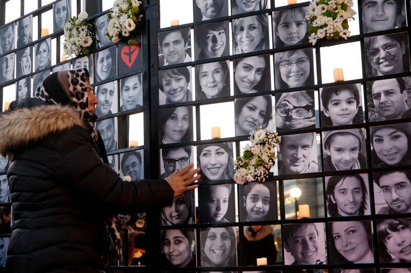 A woman touches victims' portraits as mourners attend an outdoor vigil for the victims of Ukrainian passenger jet flight PS752, which was shot down two years ago over Iran, in Toronto, Ontario, Canada, January 8, 2022.  - Ukraine International Airlines flight PS752 was shot down shortly after take-off from Tehran's Imam Khomeini airport on January 8, 2020, killing all 176 people on aboard.  Most were Iranians and Canadians, including many dual nationals.  (Photo by Cole Burston  /  AFP)