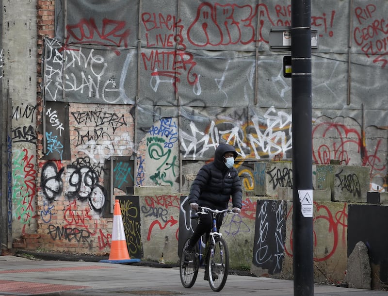 A cyclist wears a mask as he passes graffiti in London during England's third national lockdown. AP Photo