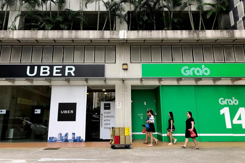 Office workers walk past Grab and Uber offices during their lunch hour Monday, March 26, 2018, in Singapore. Grab, a fast growing Southeast Asian ridesharing, food delivery and financial services business, said Monday that Uber will take a 27.5 percent stake in it and a seat on its board as part of the deal. (AP Photo/Wong Maye-E)