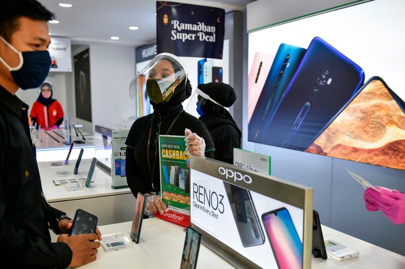 An employee of a smartphone shop (C) wears a face mask under a protective face shield to combat the spread of the COVID-19 coronavirus as she speaks to a customer at a market in Banda Aceh on May 28, 2020. / AFP / CHAIDEER MAHYUDDIN
