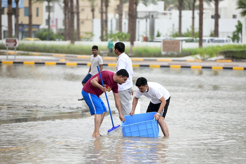 Staff at a restaurant scoop up water surrounding the premises in Fujairah. Khushnum Bhandari / The National