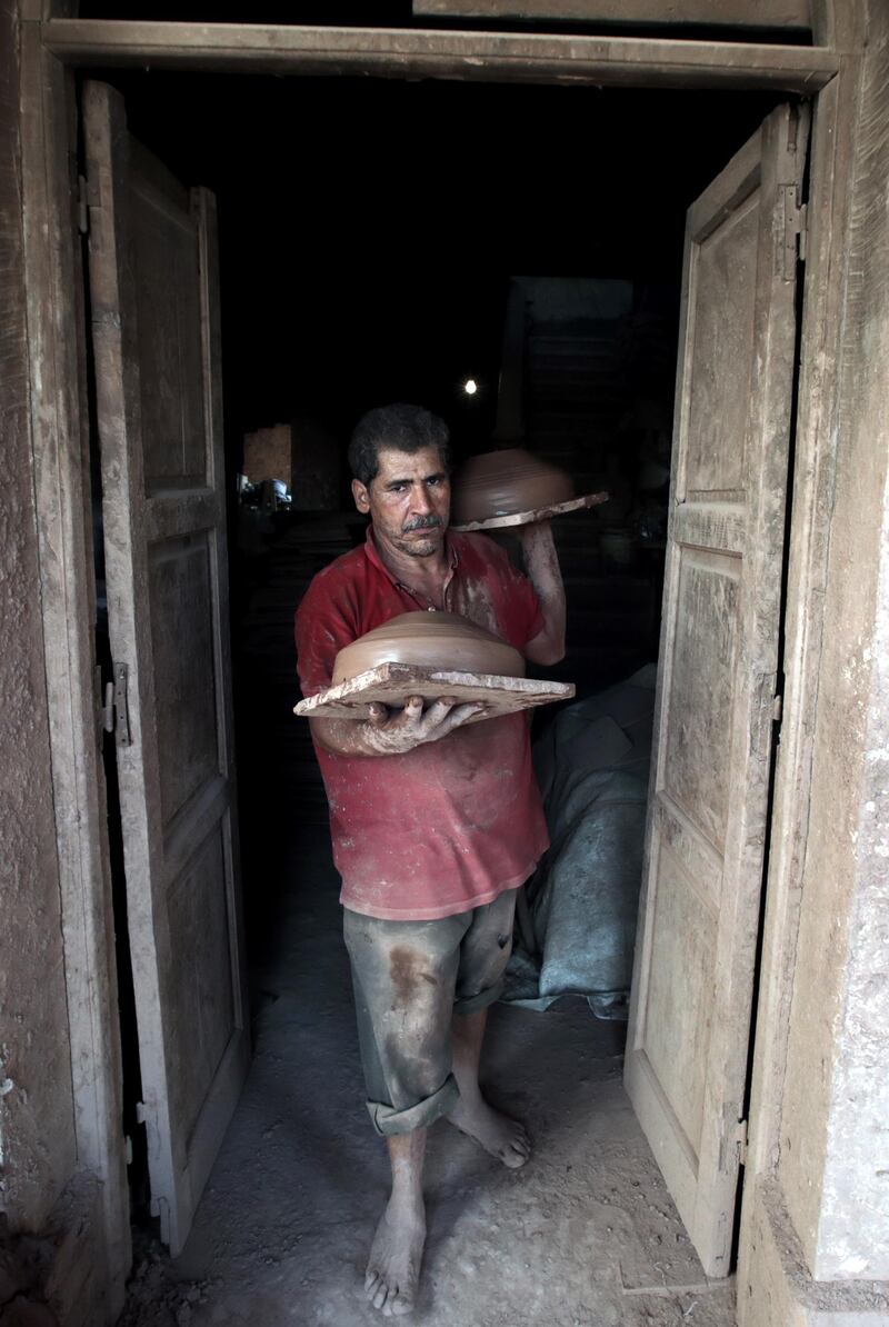 An Egyptian worker carries clay pots to be dried before displaying them for sale.