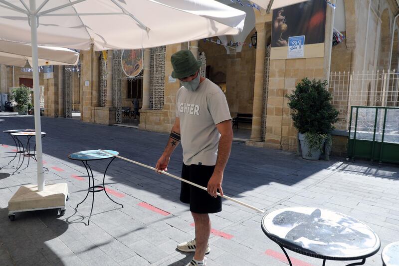 A man measures the distance between tables at a cafe as businesses reopen in Nicosia, Cyprus. EPA