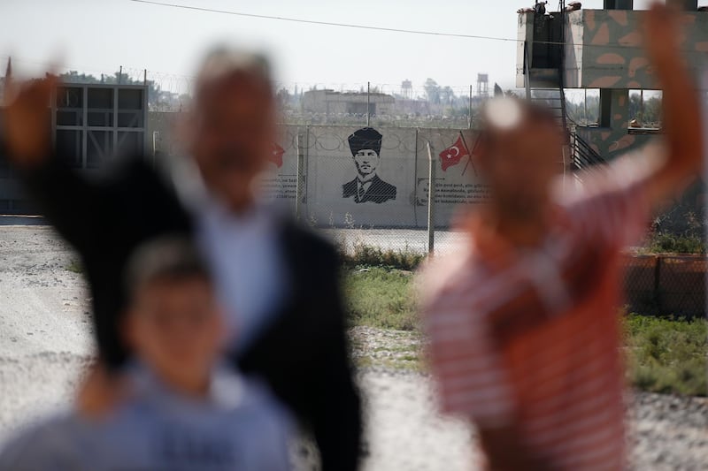 Backdropped by a graffiti depicting modern Turkey's founder Mustafa Kemal Ataturk, supporters of Turkey's Nationalist Movement Party (MHP) pose for photos at the border between Turkey and Syria, in Akcakale, Sanliurfa province, southeastern Turkey. AP Photo