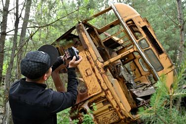 A visitor takes a picture at a wreckage of a bus in the ghost city of Pripyat during a tour in the Chernobyl exclusion zone. Courtesy AFP