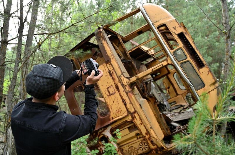 TOPSHOT - A visitor takes a picture at a wreckage of a bus in the ghost city of Pripyat during a tour in the Chernobyl exclusion zone on June 7, 2019. HBO’s hugely popular television series “Chernobyl” has renewed interest around the world on Ukraine’s 1986 nuclear disaster with authorities reporting a 30% increase of tourist demands to visit the affected area and tourist operators forecasting that number of tourists visiting the site may double this year up to 150.000 persons / AFP / Genya SAVILOV
