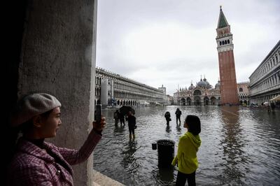 TOPSHOT - Tourists take photos on the flooded St. Mark's Square, by the Bell Tower (Rear R) and St. Mark's Basilica (Rear C) on November 24, 2019 in Venice during a high tide "Acqua Alta" meteorological phenomenon with a high of 140 cm expected. Flood-hit Venice was bracing for another, though smaller, high tide on November 24, after Italy declared on November 15 a state of emergency for the UNESCO city where perilous deluges have caused millions of euros worth of damage. / AFP / Miguel MEDINA
