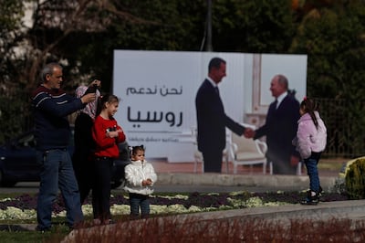 A family stands near a billboard showing Russian President Vladimir Putin and Syrian President Bashar Assad in Damascus in March. AP Photo