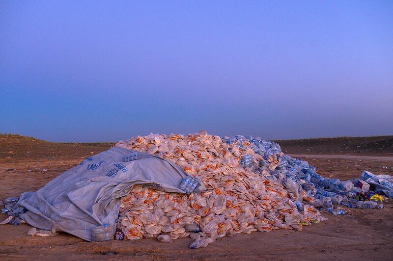 This picture taken on March 9, 2019 shows a pile of food aid composed of bread and water bottles in the desert, left for new coming civilians out of the town of Baghouz, in the eastern Syrian province of Deir Ezzor. - More than 7000 people, mostly women and children, have fled the shrinking pocket over the past days, as US-backed forces press ahead with an offensive to crush holdout jihadists. (Photo by BULENT KILIC / AFP)