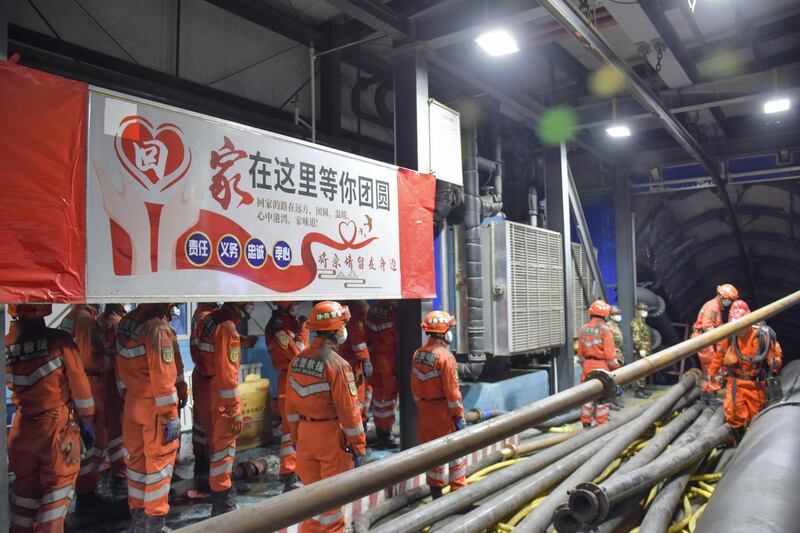 In this photo released by Xinhua News Agency, rescue workers stand near a banner which reads: "Home is waiting for your region" at the entrance to a flooded coal mine in Hutubi county in of Hui Autonomous Prefecture of Changji, northwest China's Xinjiang Uyghur Autonomous Region on Sunday, April 11, 2021. Some miners were reported trapped after the coal mine flooded on Saturday. (Gao Han/Xinhua via AP)