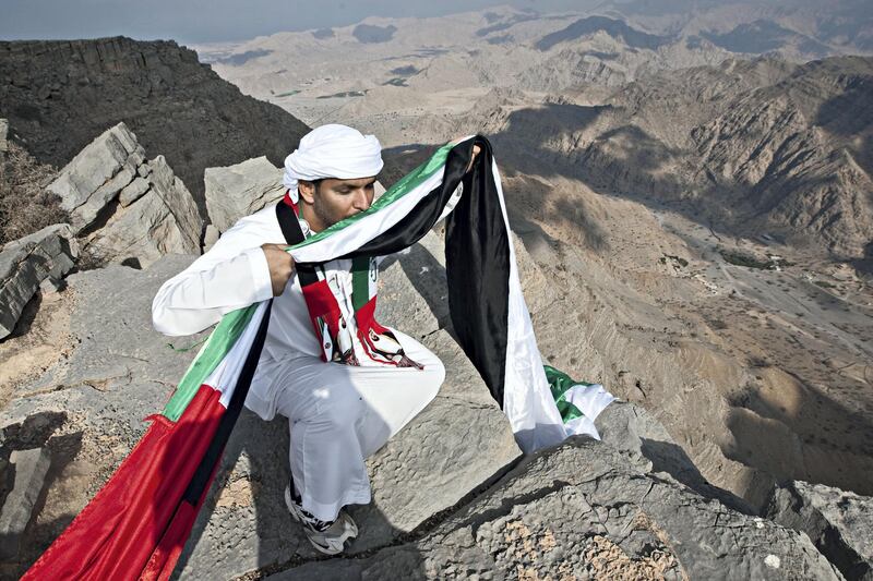 Ras al Khaimah, December 1, 2011 - Ahmed Bin Shaiban Al Hebsi, 35, kisses a portion of the 40-meter long UAE flag he and his brothers carried to the top of Jebel Janas to hang over the ledge above Wadi Qada'a where their father lives near Ras al Khaimah City, in Ras al Khaimah, December 1, 2011. Several attempts were made to hang the flag but a weak wind caused them to move to a different location. (Jeff Topping/The National)