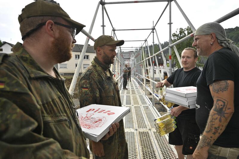Local residents hand out pizzas to members of the German armed forces  at a temporary bridge built over the River Ahr, near Bad Neuenahr, Rhineland-Palatinate.