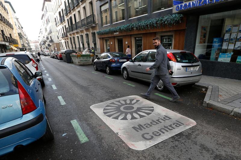 A man looks at a sign painted on the road indicating the boundary of the centre of the city as he crosses the street in Madrid, Spain, Friday, Nov. 30, 2018. Madrid activated a new traffic restriction system Friday in an attempt to reduce pollution in the city. Petrol vehicles before 2000 and diesel ones registered before 2006 are banned from this central area but on the first day of the restrictions, drivers will not be fined as municipal police were only warning drivers of the new restrictions. (AP Photo/Paul White)