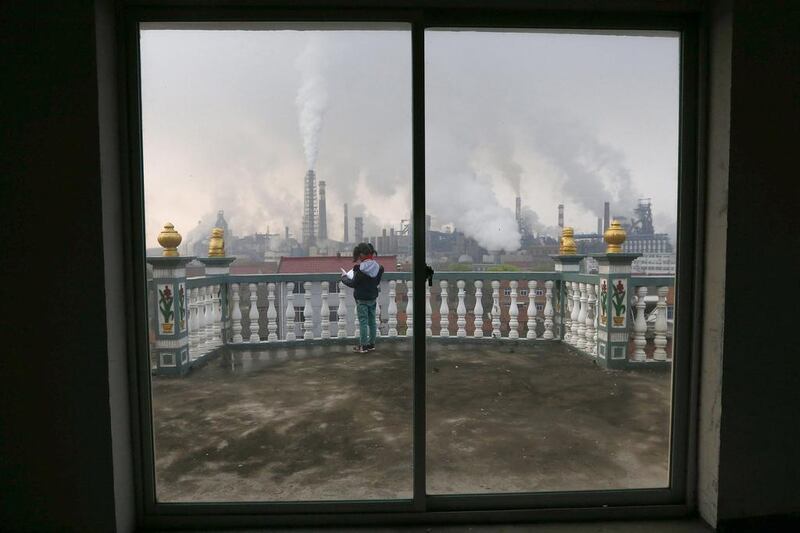 A girl reads a book on her balcony as smoke rises from chimneys of a steel plant in Quzhou, Zhejiang province. China’s plan for a market in air pollution permits promises to help clean up its air cheaply. Reuters