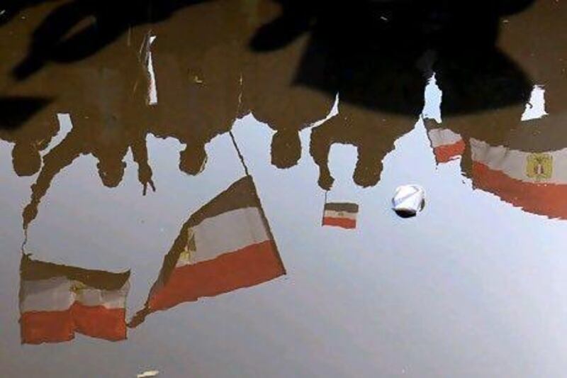 Egyptians protesters waving national flags are reflected in rain water in Cairo's Tahrir Square during a mass rally on January 25, 2012 marking the first anniversary of the uprising that toppled Hosni Mubarak, while a debate raged over whether the rally was a celebration or a second push for change. AFP PHOTO/MAHMUD HAMS