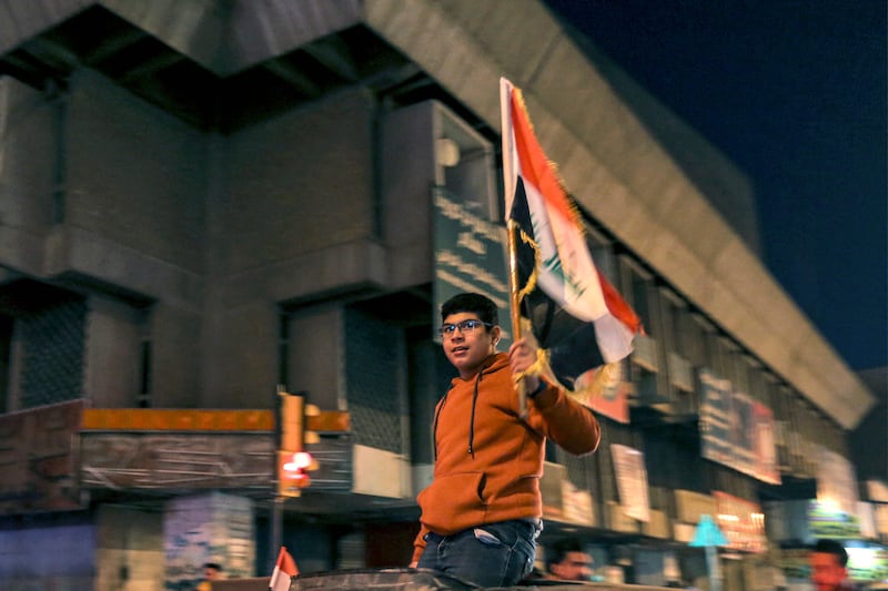 A youth waves an Iraqi flag while sitting on top of a moving vehicle in Baghdad during celebrations. AFP