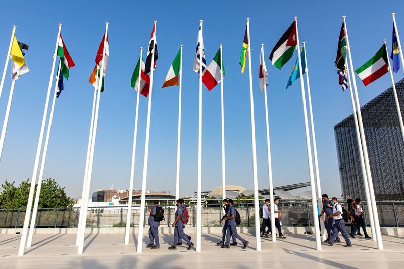 Men walk pass flags of the world's nations at the entrance to the Expo 2020 site in Dubai.  Bloomberg