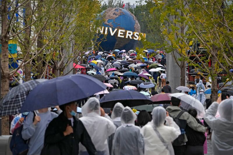 People wearing raincoats and carrying umbrellas walk through a plaza near the entrance of Universal Studios Beijing. AP Photo