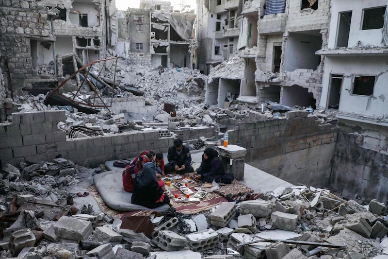 This picture taken on May 4, 2020 during the Muslim holy fasting month of Ramadan shows members of the displaced Syrian family of Tariq Abu Ziad, from the town of Ariha in the southern countryside of the Idlib province, breaking their fast together for the sunset "iftar" meal, in the midst of the rubble of their destroyed home upon their return to the town after fleeing during the previous military assault on the town by Syrian government forces and their allies.  / AFP / AAREF WATAD
