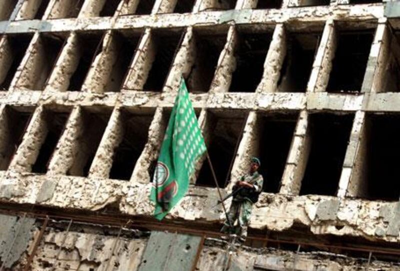 A Lebanese soldier stands in front of a building ravaged by the 1975-1990 civil war, alongside a flag for the Shiite Amal Movement.