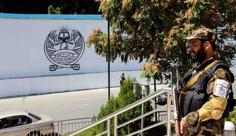 A Taliban fighter stands guard outside the former US embassy building in Kabul. On the wall opposite has been painted the group's Islamic Emirate of Afghanistan government seal. EPA