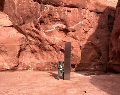FILE - In this Nov. 18, 2020, file photo provided by the Utah Department of Public Safety, a Utah state worker stands next to a metal monolith in the ground in a remote area of red rock in Utah. The mysterious silver monolith that was placed in the Utah desert has disappeared less than 10 days after it was spotted by wildlife biologists performing a helicopter survey of bighorn sheep, federal officials and witnesses said. The Bureau of Land Management said it had received credible reports that the three-sided stainless steel structure was removed on Nov. 27.  (Utah Department of Public Safety via AP, File)