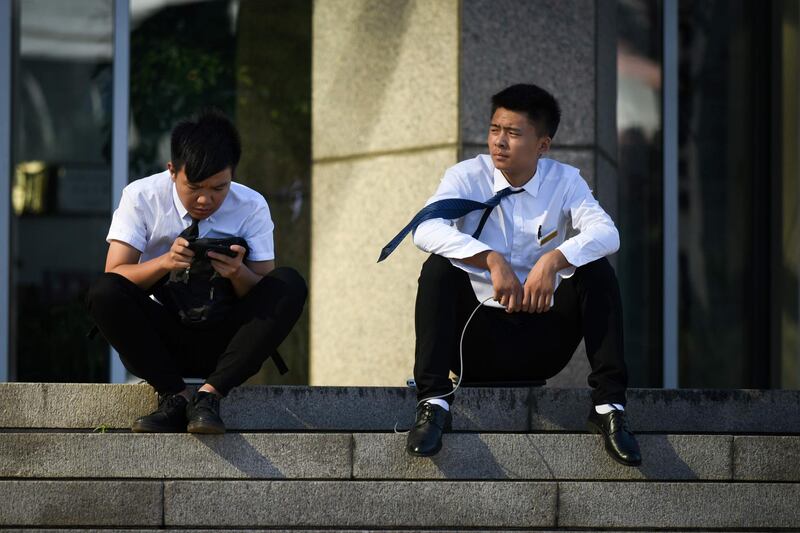 Staff members of a gym sit on the steps in front of a building in Beijing on September 3, 2018. (Photo by WANG ZHAO / AFP)