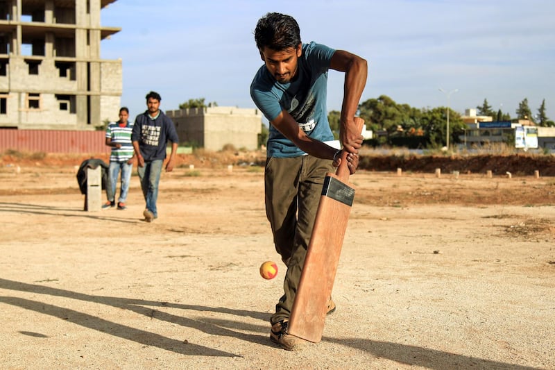 An Indian foreign worker bats a ball as he plays with others along a dirt pitch in Libya's eastern second city of Benghazi.  AFP