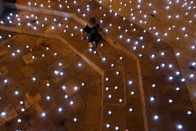 A child sits among led candles placed by activists in memory of Israel's coronavirus victims, in Jerusalem. Reuters
