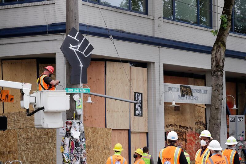 A worker prepares to remove a "Black Lives Matter St." sign and a rendering of a clenched fist from a Seattle police precinct. AP