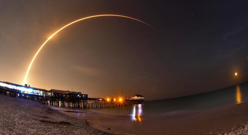 A SpaceX Falcon 9 rocket lifts off from Cape Canaveral Air Force Station with the SES-12 commercial communications satellite in Cape Canaveral, Fla., Monday, June 4, 2018. The rocket launched at 12:45 a.m. Monday morning with a satellite bound for geostationary orbit. A long exposure with a wide angle lens of the launch shows the rocket rising over the Cocoa Beach Pier in the foreground, and the waning gibbous moon rising in the east. (Malcolm Denemark/Florida Today via AP)