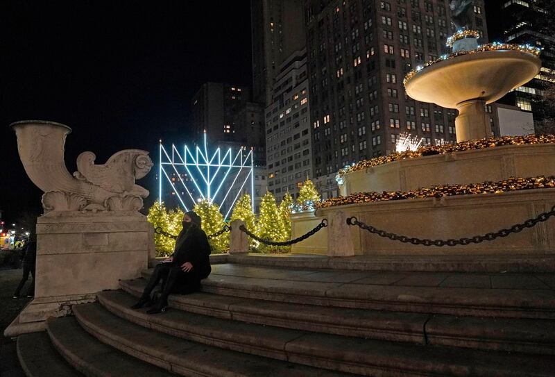 A woman sits on the steps of a fountain decorated for Christmas after the lighting of what's been described as "the world's largest Hanukkah menorah, in New York, on the first night of Hanukkah, the annual eight-day Jewish festival of lights. Due to coronavirus restrictions, a limited and socially-distanced crowd was allowed to attend. AP