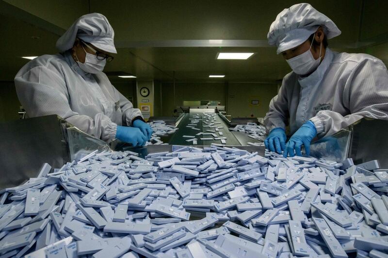 Sample testing devices used in diagnosing the Covid-19 novel coronavirus are checked on a production line as they are prepared to be included in testing kits for shipment. AFP