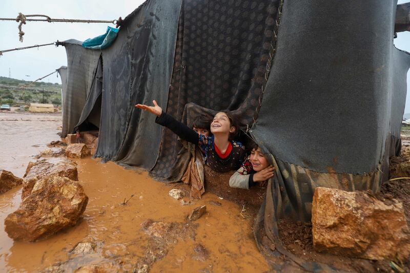 Children peek out of their flooded tent at the Umm Jurn camp for the displaced in Syria's Idlib province in January 2021. AFP