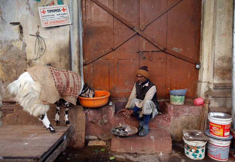 A goat, covered with a jute bag to keep warm, eats his feed as a man warms himself by a fire at a marketplace on a cold winter morning in Kolkata, India, January 10, 2018. REUTERS/Rupak De Chowdhuri