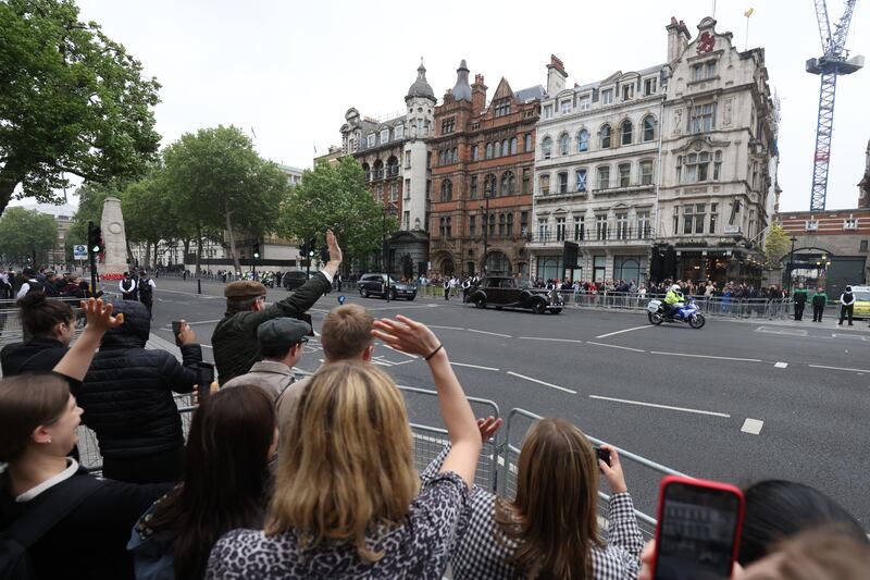 Members of the public wave at the Prince of Wales and the Duchess of Cornwall as they travel down Whitehall in central London. PA