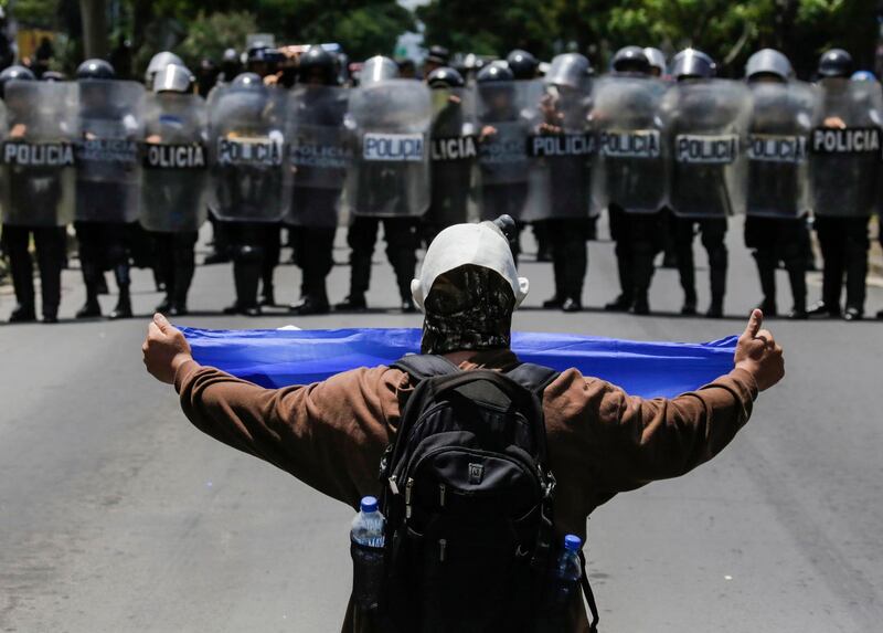 A masked demonstrator shows a Nicaraguan flag to a line of riot police blocking a street in Managua. Inti Ocon/AFP