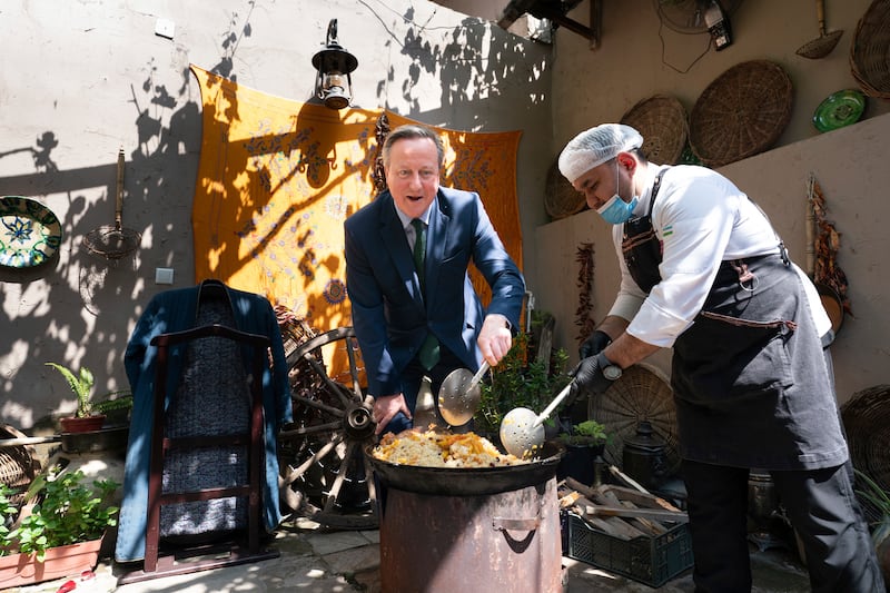 British Foreign Secretary David Cameron, left, stirs a pot of food at a restaurant in Tashkent, Uzbekistan. AP