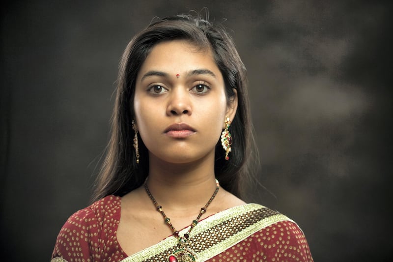 Indoor isolated image shot against dark background of a newly married Hindu young woman of Indian ethnicity looking at camera with blank expression. She is in traditional Hindu dress which is sari and blouse. One person, horizontal composition with copy space and selective focus.